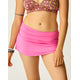A person wears the Carve Hoku Swim Skirt with an adjustable hem and a patterned bikini top, accessorized with bracelets and a tattoo on their upper arm, standing against a plain background.
