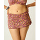 A woman models the Carve Hoku Swim Skirt—a colorful, floral-patterned skirt with adjustable hem—paired with a matching bikini top, one hand on her hip and bracelets on her wrist, shown from mid-torso to mid-thigh.