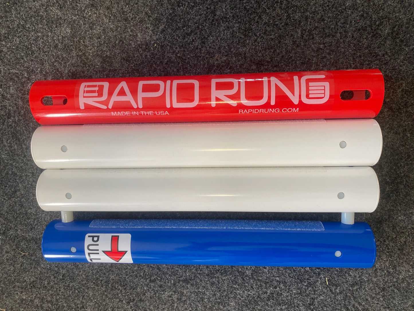 Three rungs, part of the Rapid Rung Raft Ladder, are red with "RAPID RUNG" text, white plain, and blue with a "PULL" arrow design on a gray surface, resembling a swim ladder.