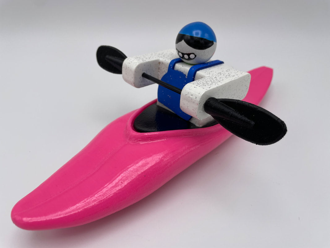 Foamie Half-Slice by Foamie Friends features a toy figure paddling a pink kayak, wearing a blue helmet and sunglasses, all set for an exciting river adventure. Photographed against a white background, this lively scene embodies the essence of water dynamics fun.
