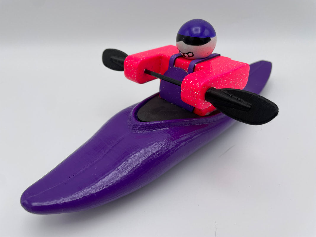 The Foamie Friends Foamie Half-Slice toy figure in a kayak is set for river adventures, equipped with a paddle. The kayak features a lively purple color, and the figure is dressed in pink, purple, and black gear.