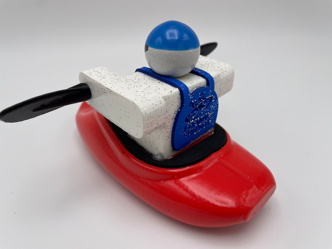 A compact Foamie Spud Play Boat from the Foamie Friends collection, featuring a white and blue figure with black paddles seated in a red kayak against a white background. Ideal for young explorers eager to learn about river dynamics with their own play boat.