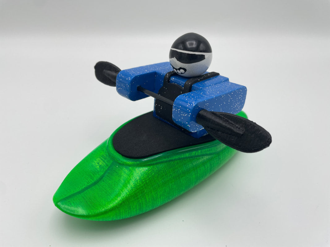 The Foamie Friends Foamie Spud Play Boat features a toy figure in a green kayak, capturing the excitement of river sports. Equipped with a black paddle and dressed in a coordinating blue and black outfit with helmet, this character is primed for adventure.