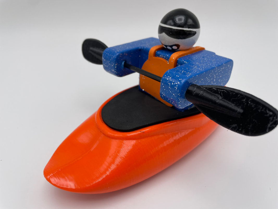 A Foamie Friends figure, part of the Foamie Spud Play Boat set, features a helmet and life vest while paddling an orange play boat with two oars, demonstrating river dynamics in action.