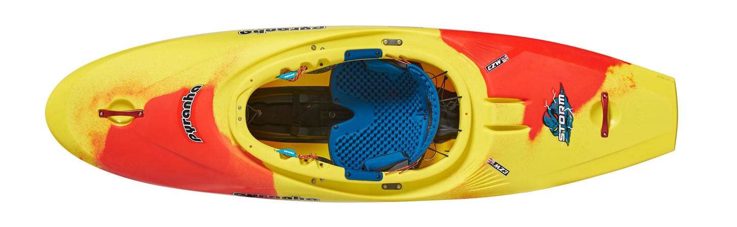 Top view of the Pyranha Storm, a vivid yellow-orange play kayak with blue seat and black footrests—ideal for downriver playboating. The deck displays the "Pyranha" logo and "Storm" branding.