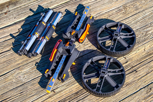 Disassembled YakAttack TowNStow BarCart Kayak Cart parts—two large black wheels, metal frame pieces, and adjustable bunk uprights—are displayed on a wooden surface.