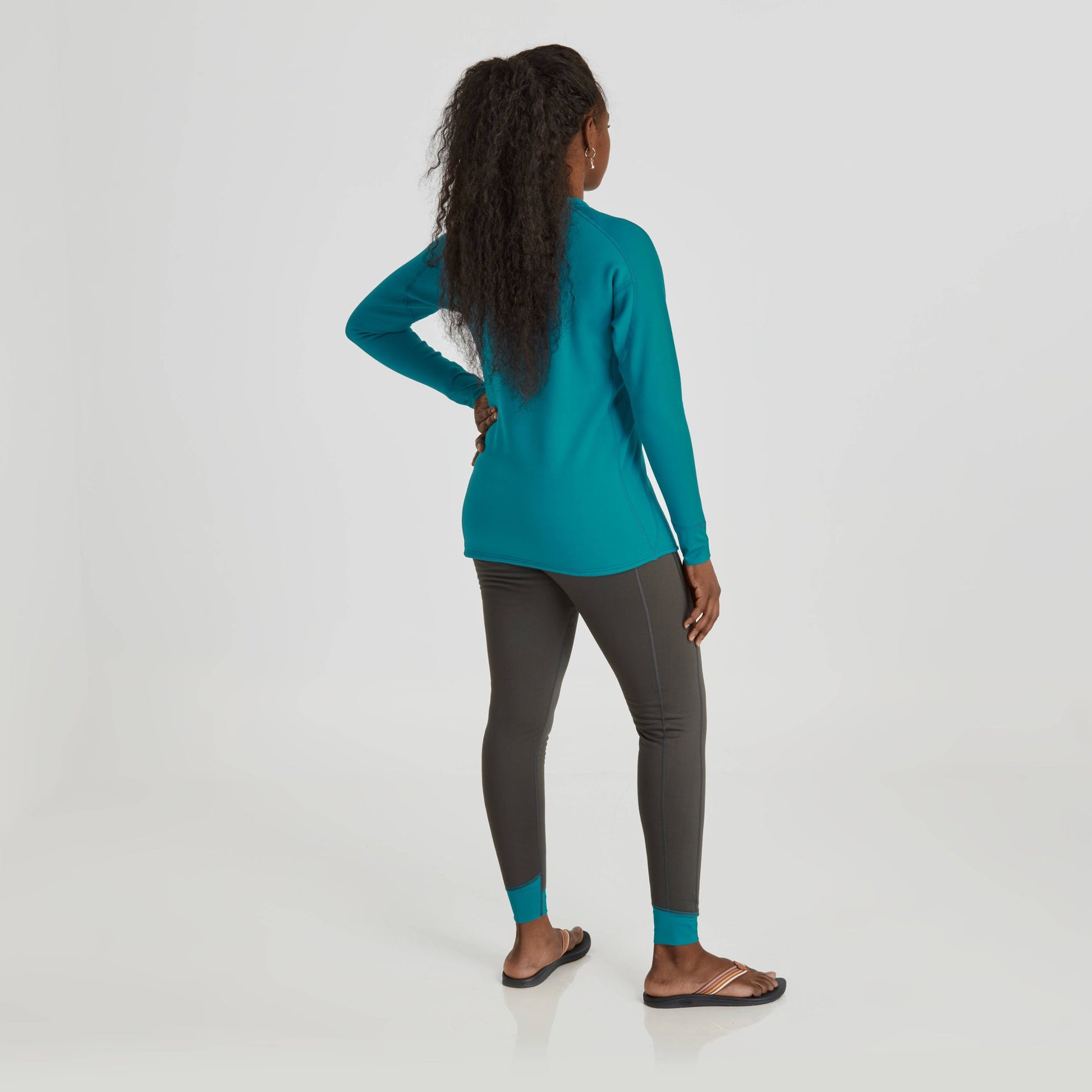 The back view of a woman wearing a teal NRS Expedition Weight Shirt - Women's and black leggings.