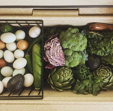 Eggs and cucumbers are in a Canyon Coolers Cooler Basket on the left, while broccoli, cabbage, kale, artichokes, avocado, and salami are neatly arranged on the right in a heavy gauge wire container.
