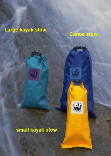 Three waterproof stow bags: a large turquoise kayak stow, a blue Canoe Stow by Jacks Plastic Welding crafted from PVC-coated polyester, and a small yellow kayak stow, all strategically placed on the rocky surface.