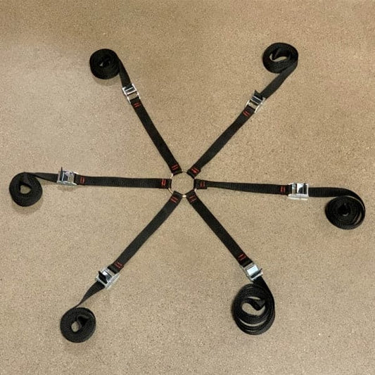 The Cargo Ant by Coyote River Gear, with black straps and a silver buckle strapping system, is stylishly arranged in a star shape on a concrete floor.