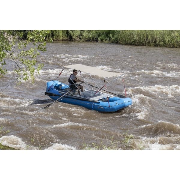 A person in a blue inflatable raft equipped with a Raft Bimini from Coyote River Gear navigates whitewater rapids, sheltered by the durable marine fabric canopy overhead.