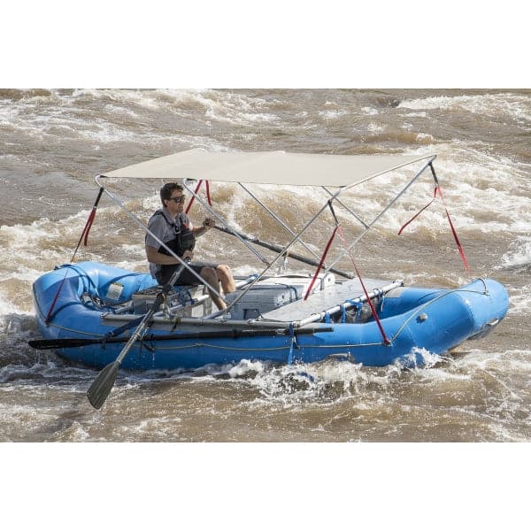 A person expertly navigates rough waters on a blue Coyote River Gear Raft Bimini, an inflatable raft with a canopy, featuring durable marine fabric.