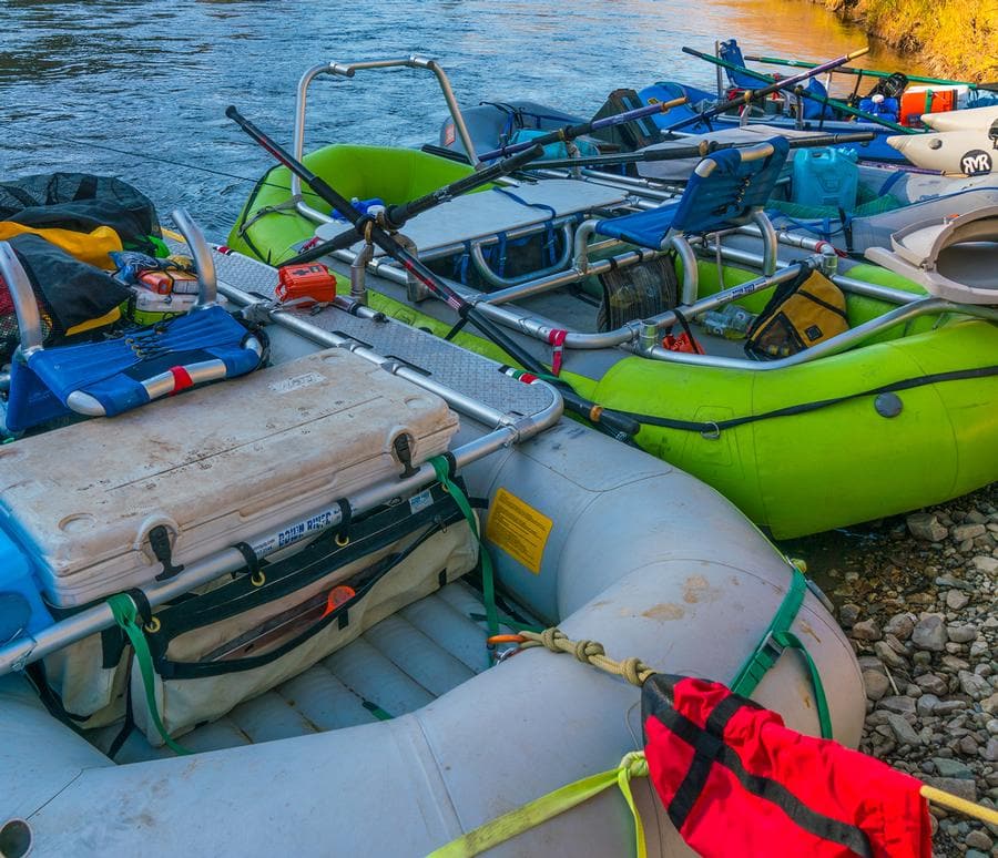 Down River Equipment's Cross Bar Bag XD, alongside cargo gear and coolers, is set up on a rocky riverbank with inflatable rafts.