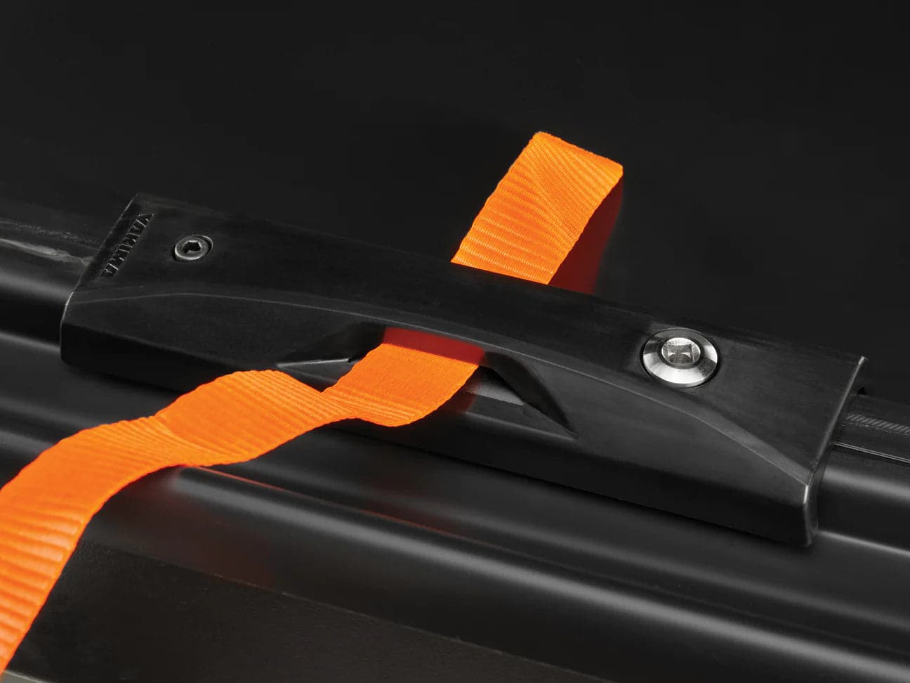 The Yakima Skybox NX XL uses a nano-texture clamp to hold an orange strap securely against a dark surface, keeping it firmly in place.