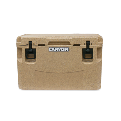 The tan PRO Series Cooler by Canyon Coolers features a textured surface, black handles, and a sleek logo on the front. Built for adventure, it offers maximum ice retention and includes a lifetime warranty for peace of mind.