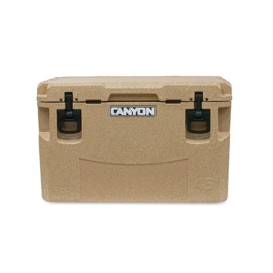 The tan PRO Series Cooler by Canyon Coolers features a textured surface, black handles, and a sleek logo on the front. Built for adventure, it offers maximum ice retention and includes a lifetime warranty for peace of mind.