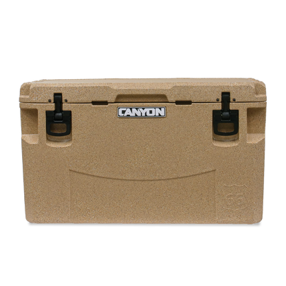 A tan PRO Series Cooler from Canyon Coolers, featuring black handles and the iconic "Canyon" logo on the lid, promises maximum ice retention.
