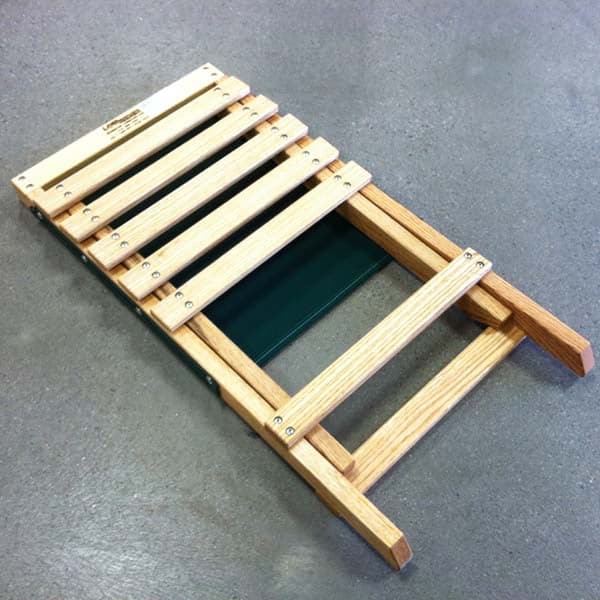 The 4CRS Lowrider Folding Chair by Coyote River Gear, featuring a wooden frame with green fabric for portable garden seating, is placed flat on a weather-resistant concrete surface.
