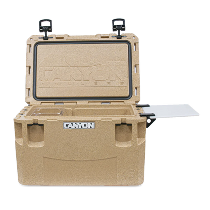The tan PRO Series Coolers by Canyon Coolers feature an open lid that reveals an insulated interior for superior ice retention. A handy cutting board is attached to the side, and it includes a lifetime warranty.